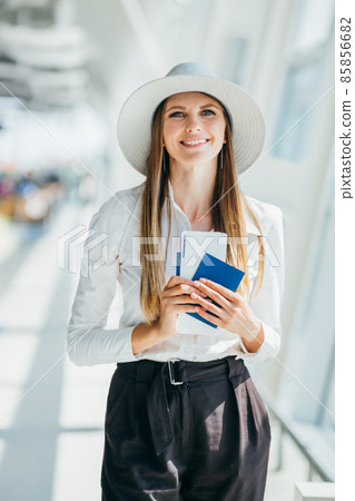 Cheerful businesswoman waiting for her flight at airport. Young woman at the airport. Young woman holding passport and boarding pass at airport. Fashion woman portrait. Businesswoman travelling by air Cheerful businesswoman waiting for her flight at airport. Young woman at the airport. Young woman holding passport and boarding pass at airport. Fashion woman portrait. Businesswoman travelling by air 85856682