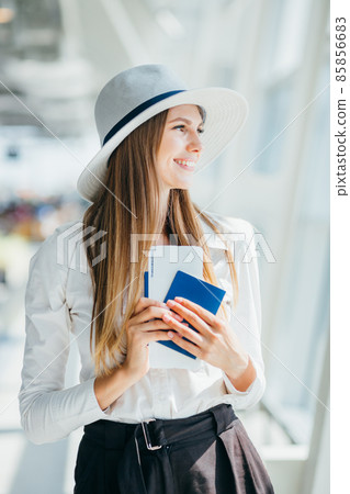 Elegant beautiful business girl holding travel tickets and using phone, happy girl looking at camera in airport terminal. Fashion woman portrait. Airport terminal. Business trip. Elegant beautiful business girl holding travel tickets and using phone, happy girl looking at camera in airport terminal. Fashion woman portrait. Airport terminal. Business trip. 85856683