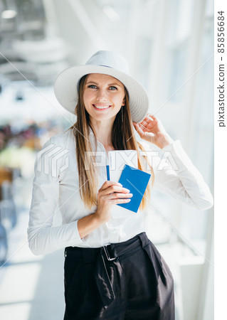 Cheerful businesswoman waiting for her flight at airport. Young woman at the airport. Young woman holding passport and boarding pass at airport. Attractive young woman going on a trip by air. Cheerful businesswoman waiting for her flight at airport. Young woman at the airport. Young woman holding passport and boarding pass at airport. Attractive young woman going on a trip by air. 85856684