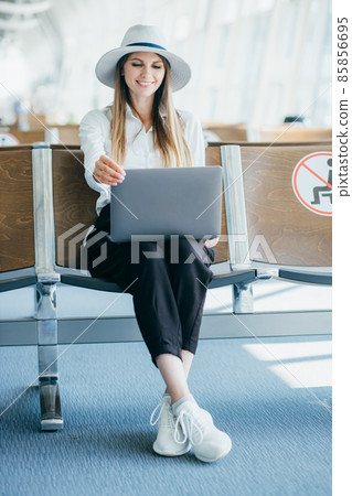 Young woman holding a laptop on lap typing keyboard indoors in airport. 85856695