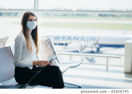 Beautiful business woman at the airport, using the phone to send text messages, standing by the window in the corporate office building, checking messages. The girl is holding tickets and a passport. 85856745