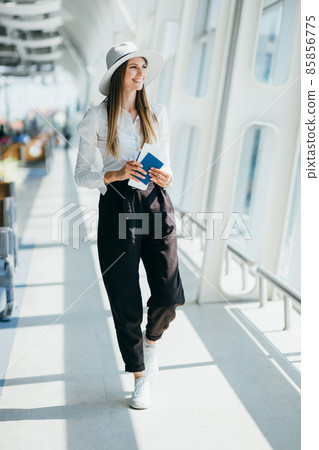 Elegant beautiful girl holding travel tickets and using a phone, happy girl looking at the camera in the airport terminal. Fashion woman portrait. Airport terminal. Business trip. Elegant beautiful girl holding travel tickets and using a phone, happy girl looking at the camera in the airport terminal. Fashion woman portrait. Airport terminal. Business trip. 85856775