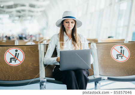Casual woman working on laptop in airport hall. Woman waiting his flight at airport terminal, sitting on chair and typing on the laptop 85857046