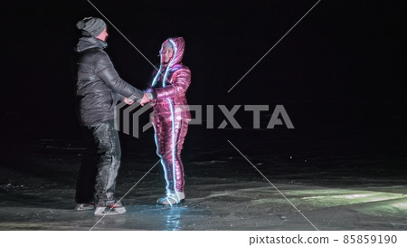 Young loving couple skating at ice rink at night. Man and woman kiss hug have fun learn to skate. Making love on ice. Ice illuminated backlit below. Young loving couple skating at ice rink at night. Man and woman kiss hug have fun learn to skate. Making love on ice. Ice illuminated backlit below. 85859190
