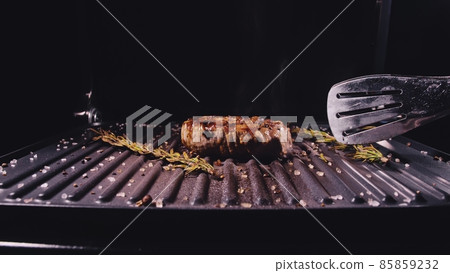 Delicious juicy meat steak cooking on grill. Aged prime rare roast grilling marble beef. Electric roaster, rosemary black pepper, salt. Kitchen tongs. Delicious juicy meat steak cooking on grill. Aged prime rare roast grilling marble beef. Electric roaster, rosemary black pepper, salt. Kitchen tongs. 85859232