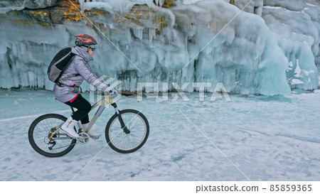 Woman is riding bicycle near the ice grotto. The rock with ice c 85859365
