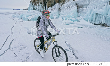 Woman is riding bicycle near the ice grotto. The rock with ice c 85859366