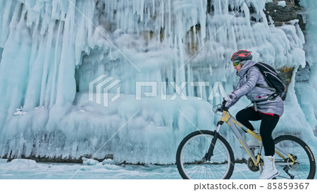 Woman is riding bicycle near the ice grotto. The rock with ice c 85859367