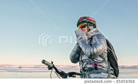 Woman is riding bicycle on the ice. Tires on bike are covered wi 85859368