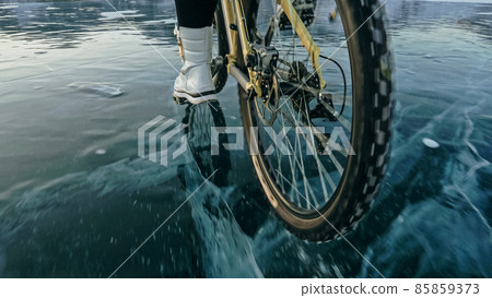 Woman is riding bicycle on the ice. Tires on bike are covered wi 85859373