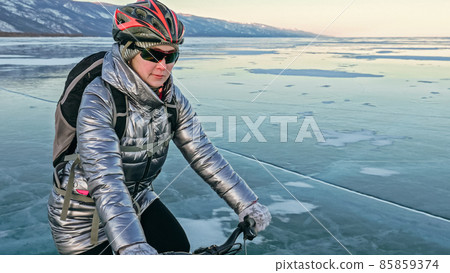 Woman is riding bicycle on the ice. Tires on bike are covered wi 85859374