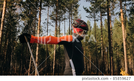 Training an athlete on the roller skaters. Biathlon ride on the roller skis with ski poles, in the helmet. Autumn workout. Roller sport. Athlete is getting ready to start. 85859627