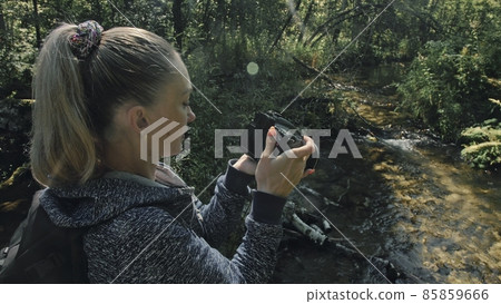 Traveler photographing scenic view in forest river. Wood bridge fallen tree. One caucasian woman shooting nice magic look. Girl take photo on camera. 85859666