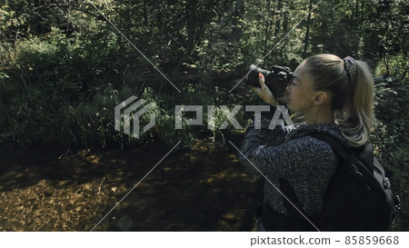Traveler photographing scenic view in forest river. Wood bridge fallen tree. One caucasian woman shooting nice magic look. Girl take photo on camera. Traveler photographing scenic view in forest river. Wood bridge fallen tree. One caucasian woman shooting nice magic look. Girl take photo on camera. 85859668