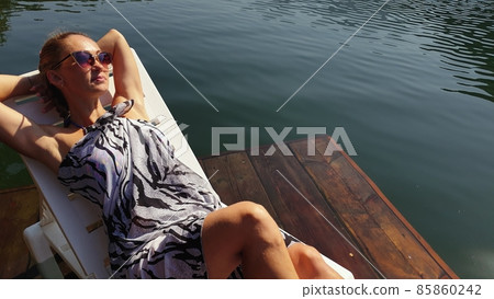 Woman lie on a sunbed in sunglasses and a boho silk shawl. Girl rest on a flood wood underwater pier. The pavement is covered with water in the lake. Woman lie on a sunbed in sunglasses and a boho silk shawl. Girl rest on a flood wood underwater pier. The pavement is covered with water in the lake. 85860242