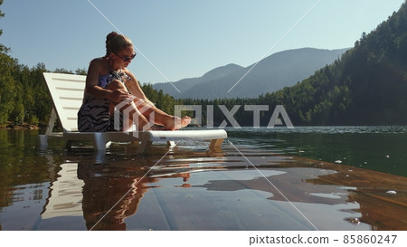 Woman lie on a sunbed in sunglasses and a boho silk shawl. Girl rest on a flood wood underwater pier. The pavement is covered with water in the lake. Woman lie on a sunbed in sunglasses and a boho silk shawl. Girl rest on a flood wood underwater pier. The pavement is covered with water in the lake. 85860247