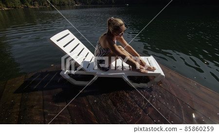 Woman lie on a sunbed in sunglasses and a boho silk shawl. Girl rest on a flood wood underwater pier. The pavement is covered with water in the lake. 85860259
