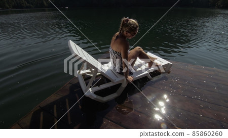 Woman lie on a sunbed in sunglasses and a boho silk shawl. Girl rest on a flood wood underwater pier. The pavement is covered with water in the lake. 85860260