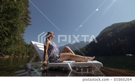 Woman lie on a sunbed in sunglasses and a boho silk shawl. Girl rest on a flood wood underwater pier. The pavement is covered with water in the lake. Woman lie on a sunbed in sunglasses and a boho silk shawl. Girl rest on a flood wood underwater pier. The pavement is covered with water in the lake. 85860264