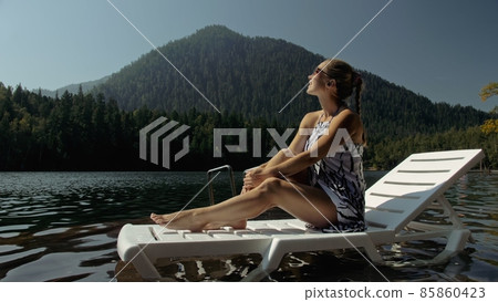 Woman lie on a sunbed in sunglasses and a boho silk shawl. Girl rest on a flood wood underwater pier. The pavement is covered with water in the lake. Woman lie on a sunbed in sunglasses and a boho silk shawl. Girl rest on a flood wood underwater pier. The pavement is covered with water in the lake. 85860423