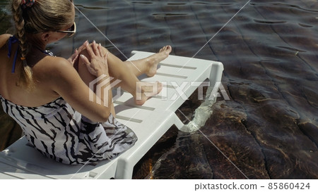 Woman lie on a sunbed in sunglasses and a boho silk shawl. Girl rest on a flood wood underwater pier. The pavement is covered with water in the lake. Woman lie on a sunbed in sunglasses and a boho silk shawl. Girl rest on a flood wood underwater pier. The pavement is covered with water in the lake. 85860424