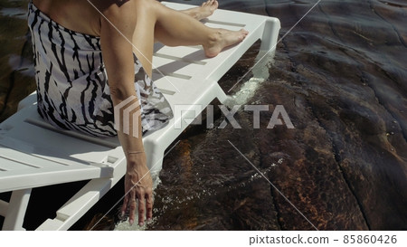 Woman lie on a sunbed in sunglasses and a boho silk shawl. Girl rest on a flood wood underwater pier. The pavement is covered with water in the lake. Woman lie on a sunbed in sunglasses and a boho silk shawl. Girl rest on a flood wood underwater pier. The pavement is covered with water in the lake. 85860426