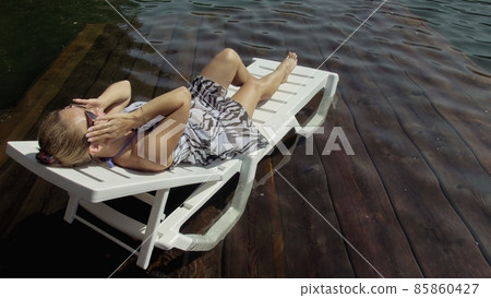 Woman lie on a sunbed in sunglasses and a boho silk shawl. Girl rest on a flood wood underwater pier. The pavement is covered with water in the lake. Woman lie on a sunbed in sunglasses and a boho silk shawl. Girl rest on a flood wood underwater pier. The pavement is covered with water in the lake. 85860427