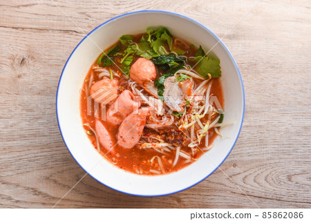 Red soup noodle pork with red roasted pork and bean sprout vegetable in soup bowl on wooden table, top view Thai and China Asian food 85862086