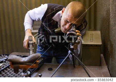 Man watching in monocle to check hitting target in shooting range Man watching in monocle to check hitting target in shooting range 85863042