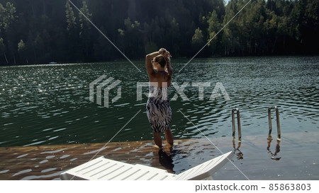 Woman lie on a sunbed in sunglasses and a boho silk shawl. Girl rest on a flood wood underwater pier. The pavement is covered with water in the lake. 85863803