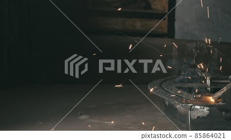 Forge workshop. Smithy. Worker in a welding hood helmet welds a part by electric welding. Sparks are reflected in the protective screen. 85864021