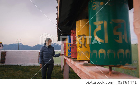 Buddhist prayer wheels drums in datsan. Woman tourist spinning a drums near the statue of the Buddha in Arshan. Buddhism. 85864471