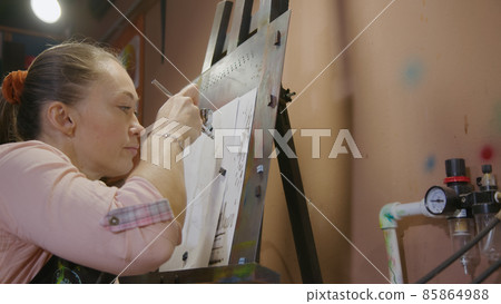 Woman artist learns to paint with airbrush with acrylic dye, paper and easel. Concept modern art, airbrushing, aerography, graffiti, aerosol spray 85864988