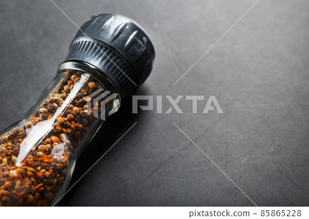 A mixture of seasonings, spices and herbs in a glass mill on a black background. 85865228