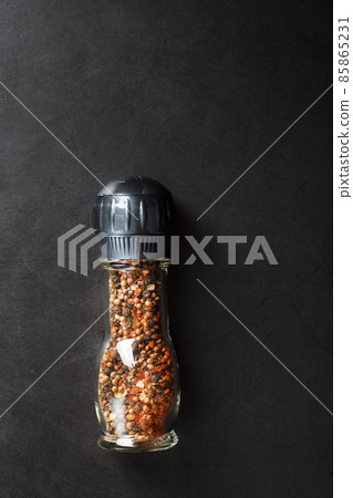A mixture of seasonings, spices and herbs in a glass mill on a black background. 85865231