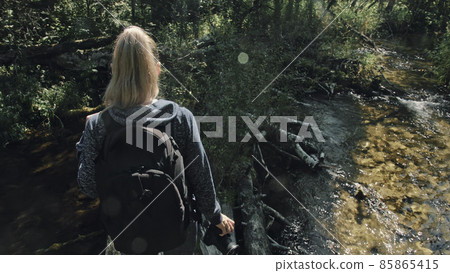 Traveler photographing scenic view in forest river. Wood bridge fallen tree. One caucasian woman shooting nice magic look. Girl take photo on camera. Traveler photographing scenic view in forest river. Wood bridge fallen tree. One caucasian woman shooting nice magic look. Girl take photo on camera. 85865415