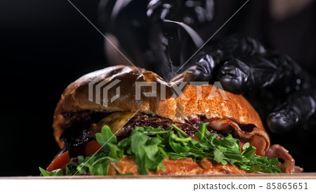 Cut craft burger is cooking on black background. Consist: sauce, lettuce, tomato, red onion, pickle, cheese, bacon, air bun and marbled meat beef. 85865651