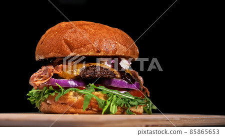 Craft burger is cooking on black background. Consist: sauce, arugula, tomato, onion, bacon, currant sauce, ricotta cheese, air bun and marble meat. Craft burger is cooking on black background. Consist: sauce, arugula, tomato, onion, bacon, currant sauce, ricotta cheese, air bun and marble meat. 85865653