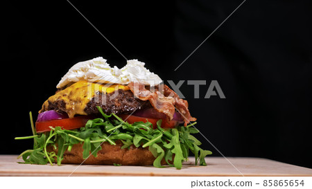 Craft burger is cooking on black background. Consist: sauce, arugula, tomato, onion, bacon, currant sauce, ricotta cheese, air bun and marble meat. 85865654