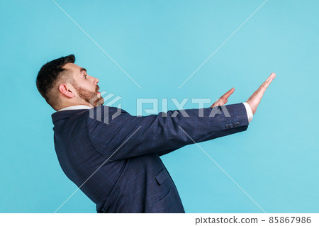 No, it's scary. Profile portrait of frightened shocked man in suit raising hands in fear, looking horrified and panicking, hiding from phobia. Indoor studio shot isolated on blue background. No, it's scary. Profile portrait of frightened shocked man in suit raising hands in fear, looking horrified and panicking, hiding from phobia. Indoor studio shot isolated on blue background. 85867986