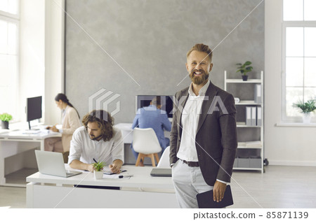 Portrait of smiling young Caucasian businessman stand in modern coworking office, employees on background. Happy successful male CEO or boss show leadership at workplace. Employment concept. Portrait of smiling young Caucasian businessman stand in modern coworking office, employees on background. Happy successful male CEO or boss show leadership at workplace. Employment concept. 85871139