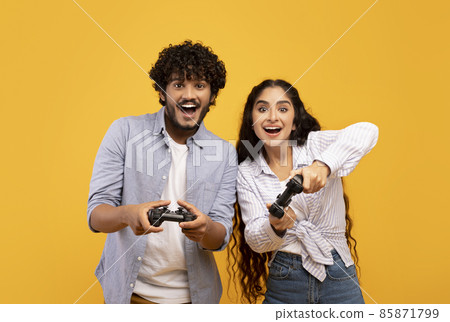 Free time entertainment concept. Joyful indian couple playing video games together, holding and using joysticks Free time entertainment concept. Joyful indian couple playing video games together, holding and using joysticks 85871799