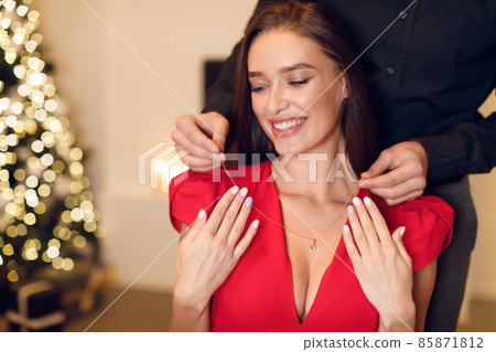 Young guy wearing luxury necklace on his happy woman Young guy wearing luxury necklace on his happy woman 85871812