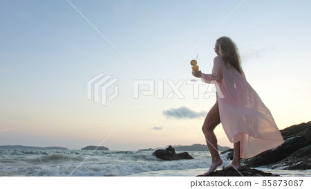Woman stand on a reef rock stone in sea on sunset. Girl on beach Woman stand on a reef rock stone in sea on sunset. Girl on beach 85873087