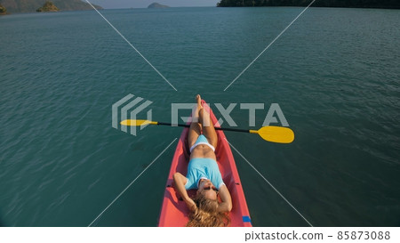Pretty slim woman in elegant swimsuit lies in pink plastic kayak drifting on azure ocean at exotic resort upper view. 85873088