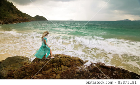 Woman walks on rock of sea reef stone, stormy cloudy ocean. Blue swimsuit dress tunic. Concept rest, tropical resort coastline tourism summer holidays 85873181