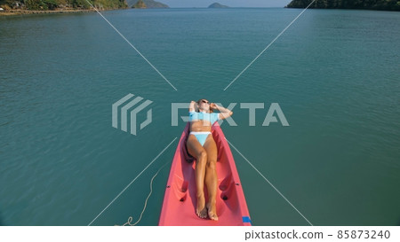 Pretty slim woman in elegant swimsuit lies in pink plastic kayak drifting on azure ocean at exotic resort upper view. 85873240