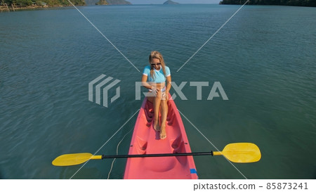 Pretty slim woman in elegant swimsuit lies in pink plastic kayak drifting on azure ocean at exotic resort upper view. Pretty slim woman in elegant swimsuit lies in pink plastic kayak drifting on azure ocean at exotic resort upper view. 85873241
