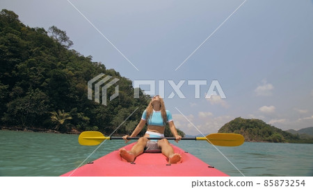Sportive woman rows pink plastic canoe along sea water. Positive sports girl hand padding on kayak, front view. Sportive woman rows pink plastic canoe along sea water. Positive sports girl hand padding on kayak, front view. 85873254