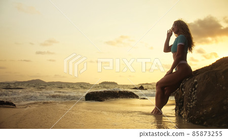 Woman leaning on a rock reef enjoying the warm golden sunset. Wo Woman leaning on a rock reef enjoying the warm golden sunset. Wo 85873255